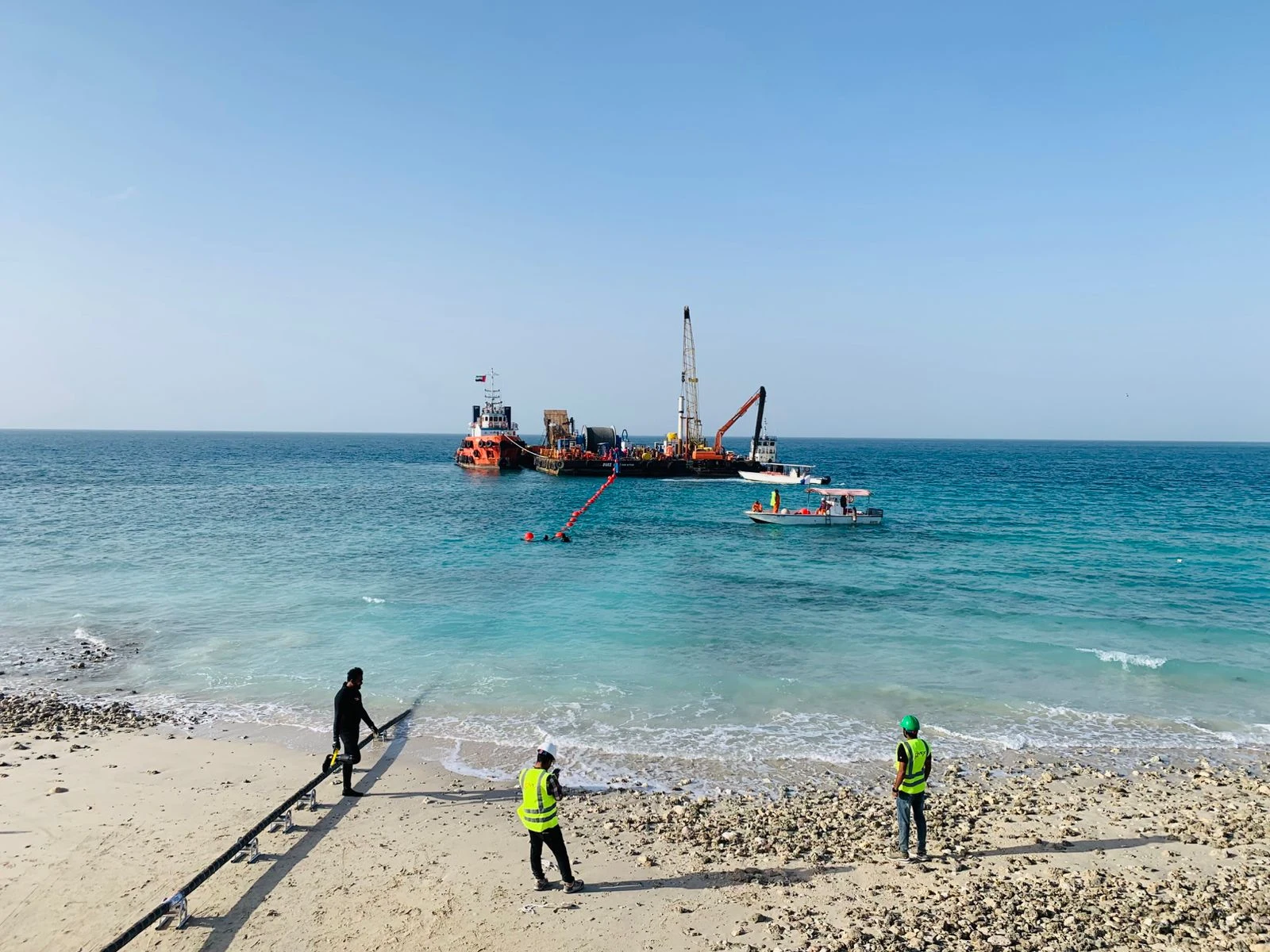 Marine construction workers on a beach beside offshore equipment and service vessels